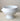 A glossy white ceramic pedestal bowl with side handles, set against a neutral beige background.