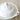 A white ceramic lidded serving dish with a decorative embossed floral knob on the lid and a side handle, photographed on a soft beige fabric background.
