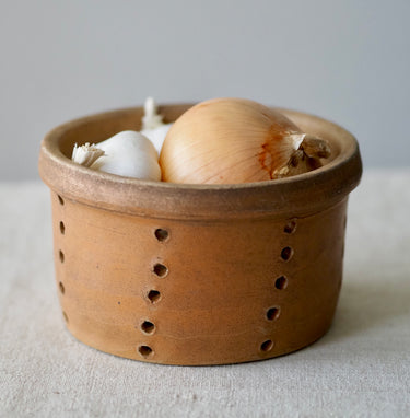 Terracotta cheese Faisselle with holes containing an onion and garlic on a neutral background
