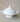 A white ceramic lidded serving dish with decorative side handles and a pedestal base, photographed against a neutral textured beige fabric background.