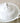 A white ceramic lidded serving dish with a decorative embossed floral knob on the lid and a side handle, photographed on a soft beige fabric background.