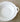 A white ceramic serving bowl with a scalloped rim and a decorative side handle, photographed from above on a textured beige fabric surface.