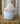 A white ceramic pot containing a decorative white coral branch, displayed on a vintage bookshelf with antique books in the background.