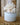 A white ceramic pot containing a decorative white coral branch arrangement, set on a rustic wooden surface with a blurred wood-paneled background.