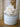 White artificial coral branch decor arranged in a small round off-white ceramic pot on a wooden surface with a softly blurred neutral background.