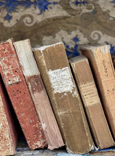 Stack of old, worn books with visible wear and tear on a patterned fabric background