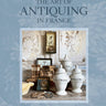 Book cover of 'The Art of Antiquing in France' by Sharon Santoni with a photo of antiques on a light blue background.
